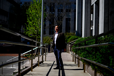 Qin Chen standing outside on a sidewalk between two buildings on Northeastern's campus 
